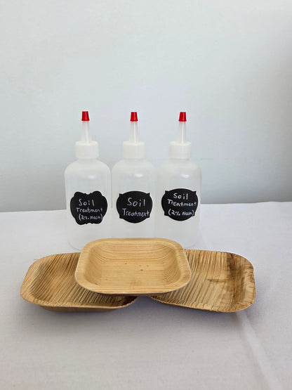 Three small bottles with red nozzles and black labels next to two wooden trays on a white surface.
